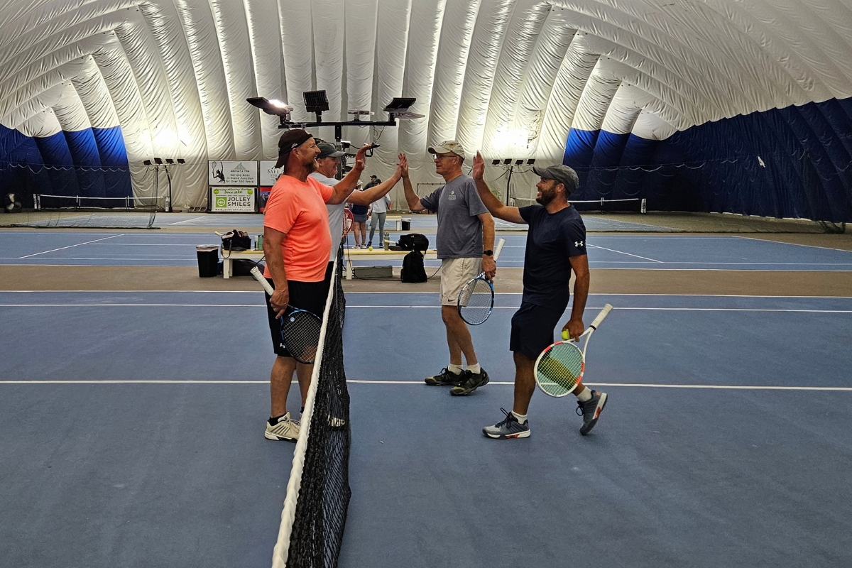 Players high-fiving at the net after a match at Junction Indoor Tennis Center